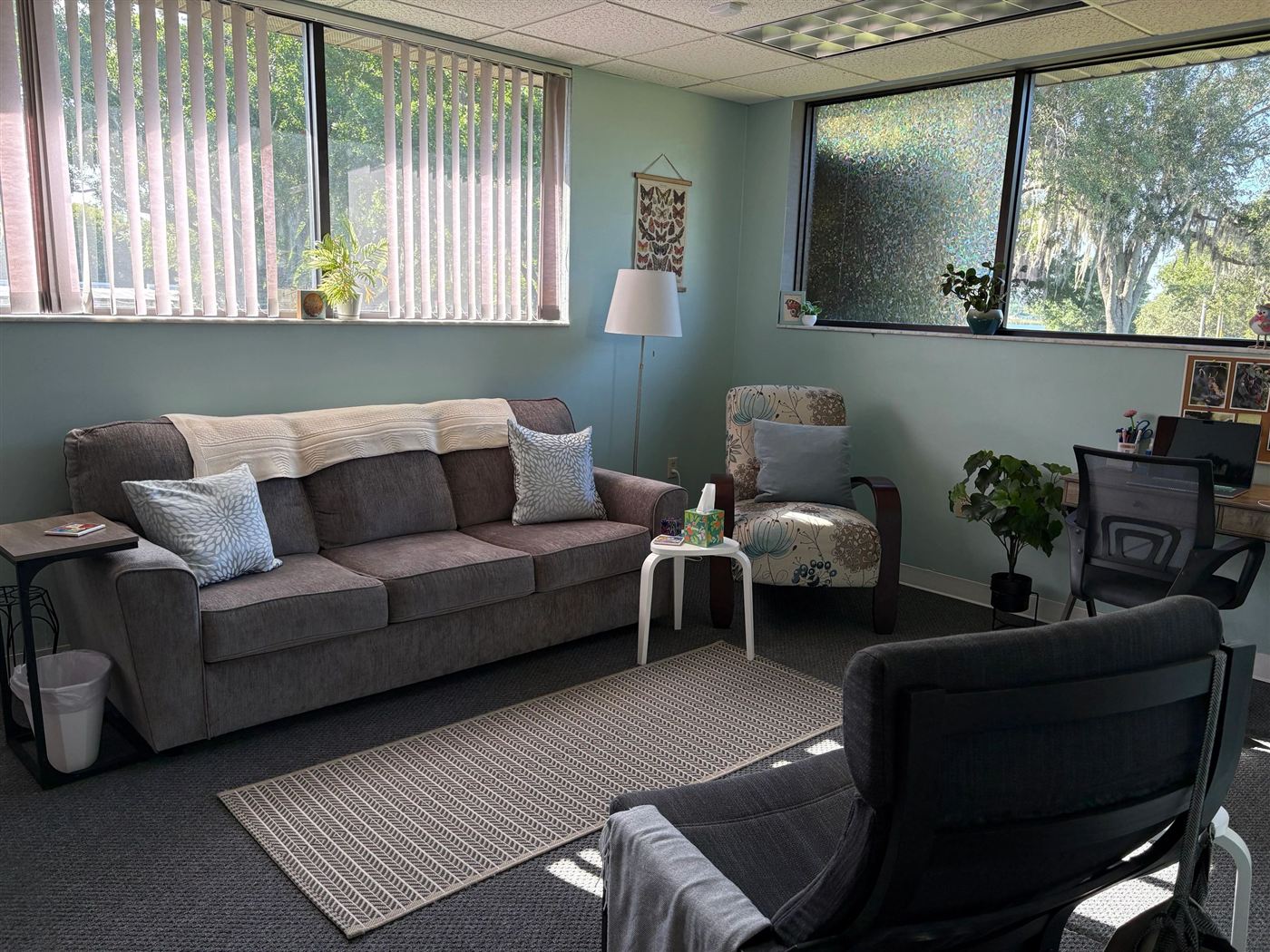 A bright counseling room at Life and Hope Counseling Center with a sofa, armchair and large windows looking out onto trees